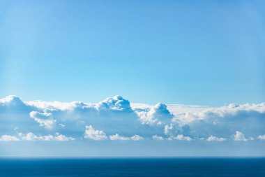 Akdeniz manzarası boyunca beyaz kabarık bulutların ve mavi gökyüzünün görüntüsü.