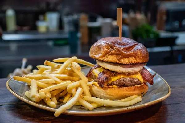 a freshly prepared bacon cheeseburger with a fried egg served with French fries.