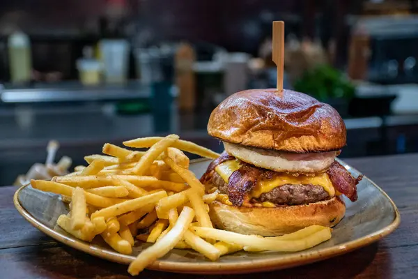 a freshly grilled angus beef cheeseburger with bacon and egg served alongside French fries.
