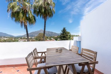 Akdeniz balkonunda ahşap bir yemek masası. Marbella 'yı çevreleyen dağı gören manzarası var. 