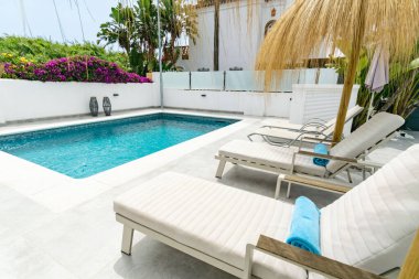 Güneşli yataklarla çevrili özel bir yüzme havuzu görüntüsü.