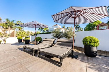 Lüks Akdeniz konak bahçesinde bir çift güneşlik ve şemsiye.