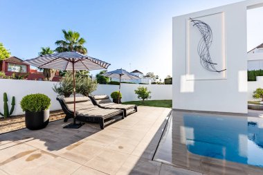 Lüks Akdeniz malikanesinde sonsuz yüzme havuzunu çevreleyen şemsiyeli bir çift güneşlik. 