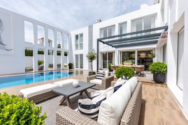 Lüks Akdeniz malikanesinde, sonsuz yüzme havuzu, çeşitli sandalyeler ve masaların yanında güneşli bir bahçe görüntüsü.