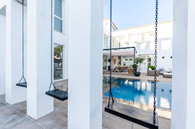 Lüks bir Akdeniz villası bahçesinde sonsuz bir yüzme havuzunun yanında üç çocuk salıncakları. 