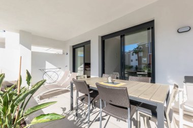 Lüks bir Akdeniz apartman balkonunda açık bir ahşap yemek masası ve güneş yatakları. 