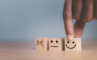 Kapalı müşteri eli gülümseme yüzü seçin ve ahşap küp, servis derecesi, müşteri hizmetleri değerlendirmesi ve memnuniyet anketleri üzerinde üzgün yüz simgesi bulanıklaştırılmış.