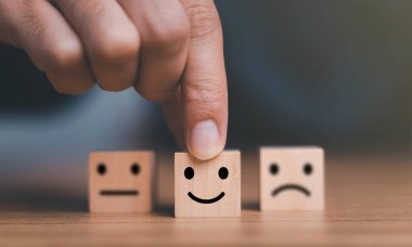 Kapalı müşteri eli gülümseme yüzü seçin ve ahşap küp, servis derecesi, müşteri hizmetleri değerlendirmesi ve memnuniyet anketleri üzerinde üzgün yüz simgesi bulanıklaştırılmış.