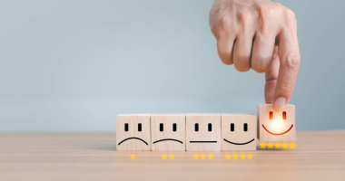 Kapalı müşteri eli gülümseme yüzü seçin ve ahşap küp, servis derecesi, müşteri hizmetleri değerlendirmesi ve memnuniyet anketleri üzerinde üzgün yüz simgesi bulanıklaştırılmış.
