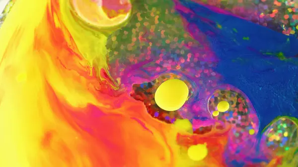 Colorful flow background. Paint blend. Spill art. Fantasy bright yellow red blue pink liquid ink abstract splash mix rotating in water with shiny sequins circles.