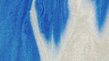 Parıltılı boya döküldü. Sıvı arkaplan. Köpüklü sıvı. Parıldayan mavi beyaz parçacıklar mürekkep akışı soyut sanat dokusuna odaklanmış..