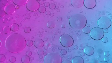 Soyut arkaplan. Yağlı su. Kabarcık dokusu. Yuvarlak lekeler, hipnotik sanatta neon mor parıldayan parçacıklar sıvı yüzey üzerinde yüzüyor..