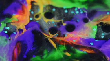 Boya karıştırma arkaplanı. Pigment karışımı lekesi. Sihirli girdaplar. Işıldayan siyah yuvarlak mor turuncu mürekkep mavi parlak pullar saçar soyut olarak yayılır..
