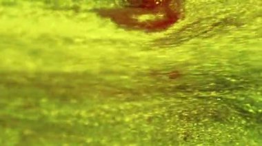 Parıldayan sıvı dökülmüş. Mürekkep suyu karışımı. Bulanık yeşil sarı kırmızı renk ışıltılı parçacıklar metalik boya akışı hareketli soyut sanat arka planı.