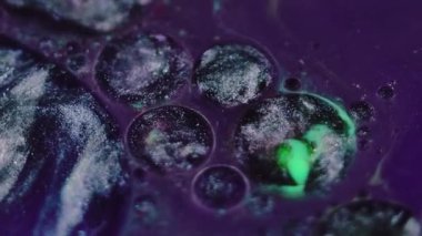 Sıvı boya arka planı. Pigment karışımı. Yağ sıvısı yüzüyor. Fantezi mor mürekkep yüzeyine yayılan yeşil lekeli parlak gri soyut yuvarlak dökülme.