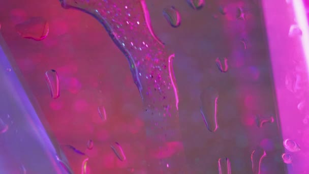 グリッターフルードリップ 水滴がこぼれる ウェットグラス 明確なボケのライトテクスチャの抽象的な芸術の背景の不分離されたネオン ピンク ブルー色光沢の純粋な雨のデュー動き — ストック動画