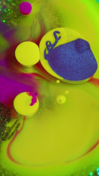 バーティカルビデオ 抽象的な背景 液体塗料ミックス グリッターインクバブル ファンタジーの活気に満ちたスプラッシュデザインアートで輝く緑の底で表面にカラフルな青い黄色の紫色の液体スポット — ストック動画