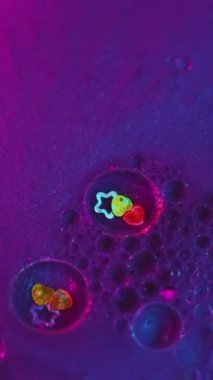 Dikey video. Işıldayan mürekkep arka planı. Sıvı sim karışımı. Banyo bombası. Canlı mavi mor sıvı renkli kozmetik tuzu pürüzsüz sabun köpükleri yıldız kalbi dekoratif parçacıkları ile soyut girdap.