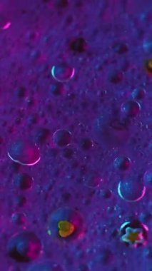 Dikey video. Mürekkep karıştırma arkaplanı. Parıltılı boya. Akışkan pullar sanat eseri. Mor mavi renkli sıvı hava kabarcıkları boyada parıldayan parçacıklar soyut hipnotik akışı harmanlıyor.