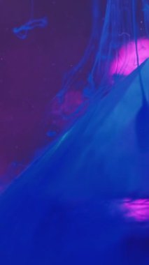 Dikey video. Mürekkep bırakma arkaplanı. Sıvı pigmenti. Soyut sis. Geometrik mor bokeh tasarımlı şeffaf kristal taş piramidin üzerindeki floresan mavi renk sıvısı buharı su hareketi.