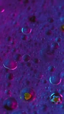 Dikey video. Mürekkep karıştırma arkaplanı. Parıltılı boya. Akışkan pullar sanat eseri. Mor mavi renkli sıvı hava kabarcıkları boyada parıldayan parçacıklar soyut hipnotik akışı harmanlıyor.