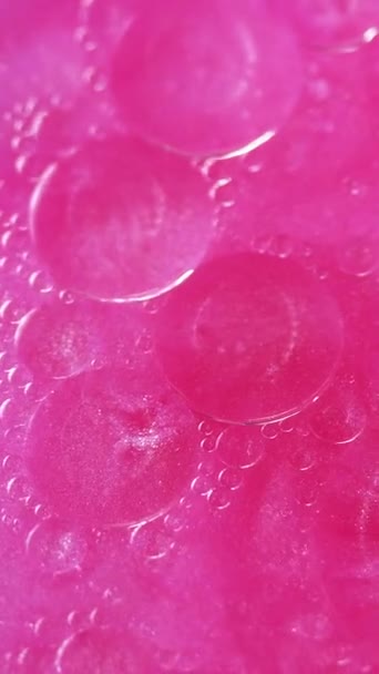 バーティカルビデオ 抽象的な背景 バブル液体 オリーの表面 クリエイティブな魅惑的な芸術のネオンピンクの輝く輝く水に広がる透明なドロップサークル — ストック動画
