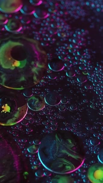 バーティカルビデオ 抽象的な背景 バブルを混ぜる カラフルなオイル水 紫色の黄色い輝く円は催眠術の創造的な液体アートのネオン輝きで動きます — ストック動画