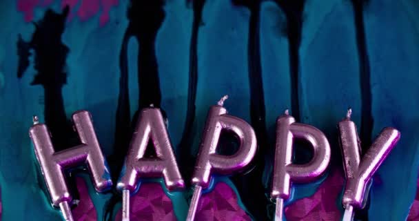 バースデーキャンドル ハッピー ホリデー インクドリップ お祝いのフォント ピンクの表面の抽象的な芸術の背景に青い黒い色のペンキのこぼれが付いている虹彩の光のライトの金属の光沢のあるワックスの手紙 — ストック動画