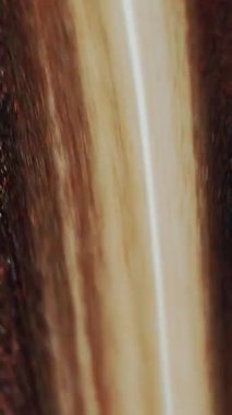 Dikey video. Parlak mürekkep damlası. Boya dökülüyor. Odaklanmamış bronz kahverengi beyaz renk parıldayan parçacıklar dokusu sıvı akışı hareket soyut sanat arkaplanı.