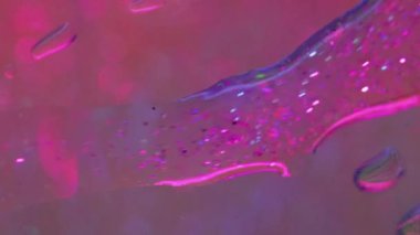 Parıldayan jel damlası. Işıldayan su döküldü. Camdan nem. Bulanık neon mavisi parlak pembe yağ emülsiyon akışı temiz bokeh hafif doku soyut sanat arka planı.