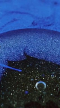 Dikey video. Soyut arkaplan. Sıvı sanat dokusu. Yağlı sıvı leke. Mavi simli parçacıklara yayılan şeffaf yağ lekesi. Altında siyah pullar olan mürekkep yüzeyi..