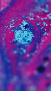 Dikey video. Işıldayan sıvı arka plan. Parıltılı boya. Akrilik boya hareketi. Mavi pembe pigment akıntısı ve siyah yuvarlak lekeler moda ve soyut sanatta yüzüyor..