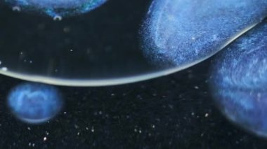 Jel damlası. Parıldayan kabarcıklar. Odaklanmamış mavi renk şeffaf ışıldayan parçacıklar desen mürekkep daireleri koyu siyah soyut sanat arka planında suda yüzüyor..