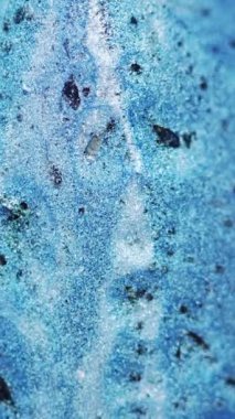 Dikey video. Işıldayan mürekkep arka planı. Islak pigment. Parlak akış. Parlak mavi sıvı ve siyah madde yüzeyde yayılıyor soyut bir harmanla..