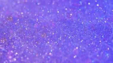 Parlak sıvı. Parıltılı boya akışı. Odaklanmamış mor renkli parıldayan pullu parçacıklar yarı saydam su sıvısı emülsiyonunda titreşiyor. Bokeh ışıklarıyla soyut sanat arka planında hareket yayılıyor..