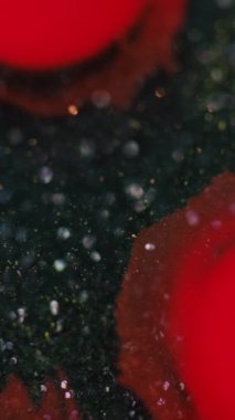 Dikey video. Mürekkep damlası. Boya serpintisi. Koyu siyah simli parçacıklarda odaksız kırmızı renk lekeli lekeli hareket soyut arkaplan efektini ortaya çıkarıyor.