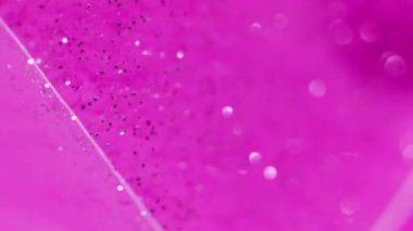 Köpüklü sıvı. Soyut arkaplan. Islak sim akışı. Bulanık renkli pembe sıvı akış beyaz parıldayan parçacıklar yüzey kenarında damlalar.
