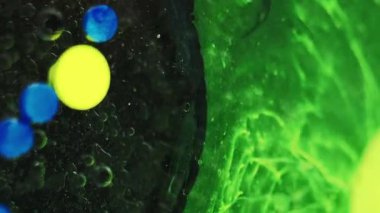 Mürekkep sıçraması. Yağ lekesi. Bulanık neon yeşil sarı renk parçacıkları desen boya su karışım çemberleri koyu siyah soyut sanat arka planında akıyor.