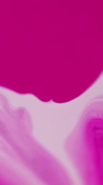 Dikey video. Mürekkep damlası. Sıvı leke. Parlak, pembe, beyaz, ıslak boya dökülmesi mavi soyut sanat arka planında açıcı hareketi yayıyor..