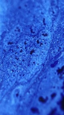 Dikey video. Parıldayan sıvı dökülmüş. Boya karışımı. Odaklanmamış mavi renkli ışıl ışıl parçacıklar sıvı mürekkep akışı kademeli hareket soyut sanat arkaplanı.