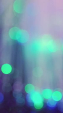 Dikey video. Neon bokeh ışığı. Odaklanmış ışınlar. Havai fişek parlaklığı. Bulanık yeşil, pembe, parlak daireler koyu soyut sanat arka planında yanıp sönen ışık deseni..