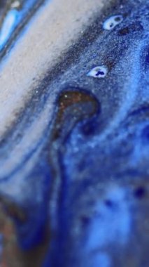 Dikey video. Parlak sıvı damlası. Mürekkep döküldü. Bulanık mavi bronz beyaz renkli metalik desenli boya emülsiyon dalgası hareketli büyüleyici soyut sanat arka planı.