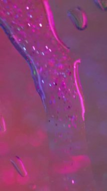 Dikey video. Parlak sıvı damlası. Su damlacıkları dökülüyor. Islak cam. Odaklanmamış neon mavi renk saf yağmur çiğ hareketi açık bokeh ışık dokusu soyut sanat arka planında.