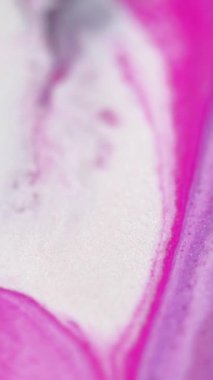 Dikey video. Mürekkep döküldü. Parıltılı boya akışı. Odaklanmamış parlak pembe beyaz renk parıldayan doku sıvı parlatıcı dalga hareketini soyut sanat arkaplanı.