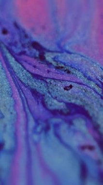 Dikey video. Boya dökülmüş. Parlak mürekkep damlası. Odaklanmamış neon mavisi mor renkli parıldayan desen sıvısı karışımı dalgalar kademeli hareket soyut sanat arkaplanı.