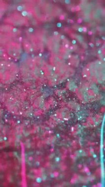 Dikey video. Işıldayan sıvı. Parlak doku. Pembe metalik soyut arkaplan yağlı zaman akışı parlak kırmızı mavi yansımalar bulanık.