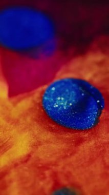 Dikey video. Islak sim sıçraması. Su karışımı boya. Odaklanmamış parlak turuncu mavi renk parıldayan parçacıklar desen mürekkep baloncukları koyu siyah soyut sanat arka planında akış hareketi.