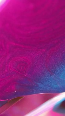 Dikey video. Parlak yağ. Parlak akış. Pembe mavi parlayan sıvı cam kristal prizma dokusuna dökülüyor. Soyut arkaplan, karışık ışıltı bokeh ışıkları bulanıklaştırıyor..