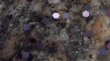 Dikey video. Parıldayan su damlası. Islak mermer taş. Odaklanmamış mor renk parıldayan pullu doku siyah bej kaya soyut sanat arka planında şeffaf sıvı akışı.