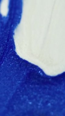 Dikey video. Mürekkep döküldü. Parıltılı boya karışımı. Odaklanmamış mavi beyaz renk ışıl ışıl parçacıklar akrilik sıvı dökülmüş parlatıcı harmanlanmış hareket soyut sanat arka planı.
